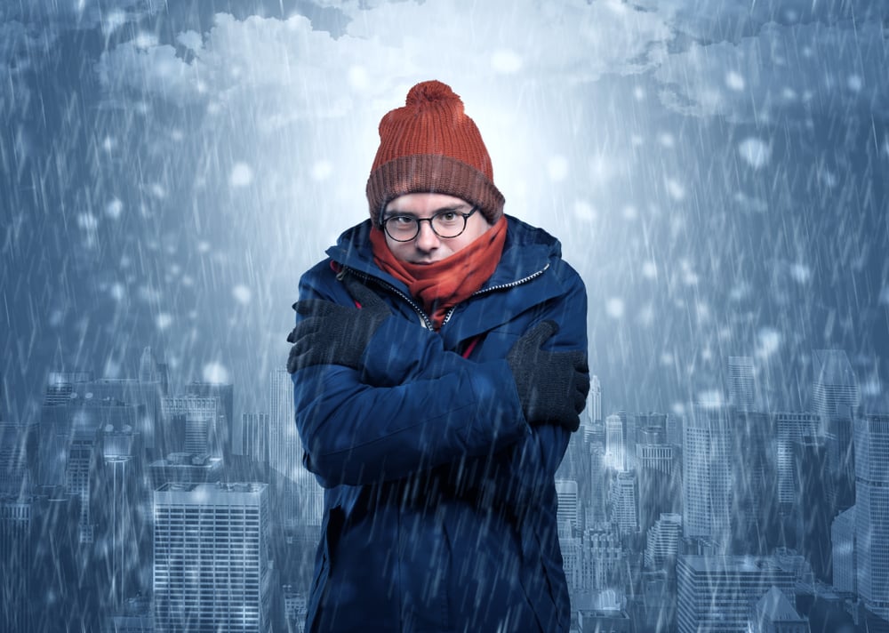 Young man freezing in warm clothing with city concept